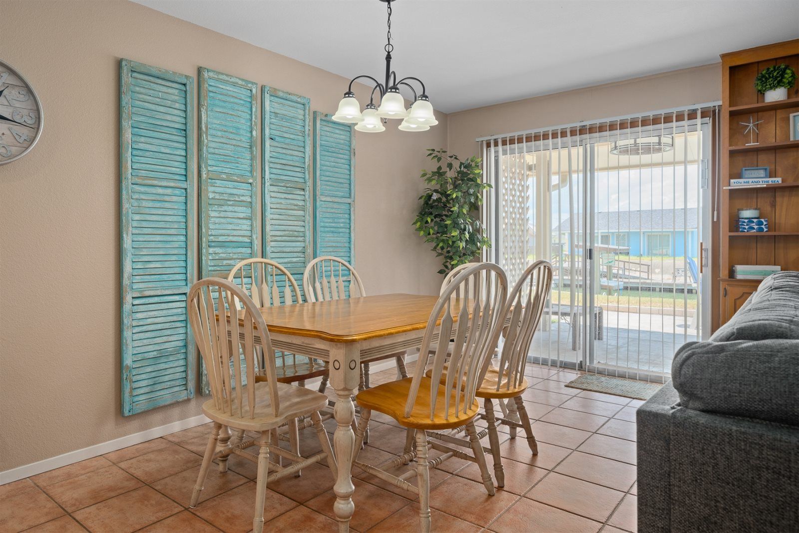 A dining area with a wooden table and chairs, a clock on the wall, and a view through a sliding glass door.