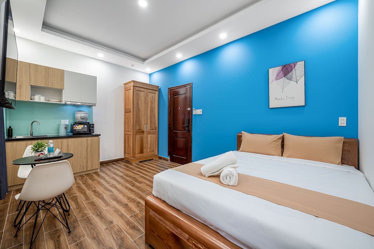 A hotel room with a bed, a desk, a kitchenette, and a bathroom.