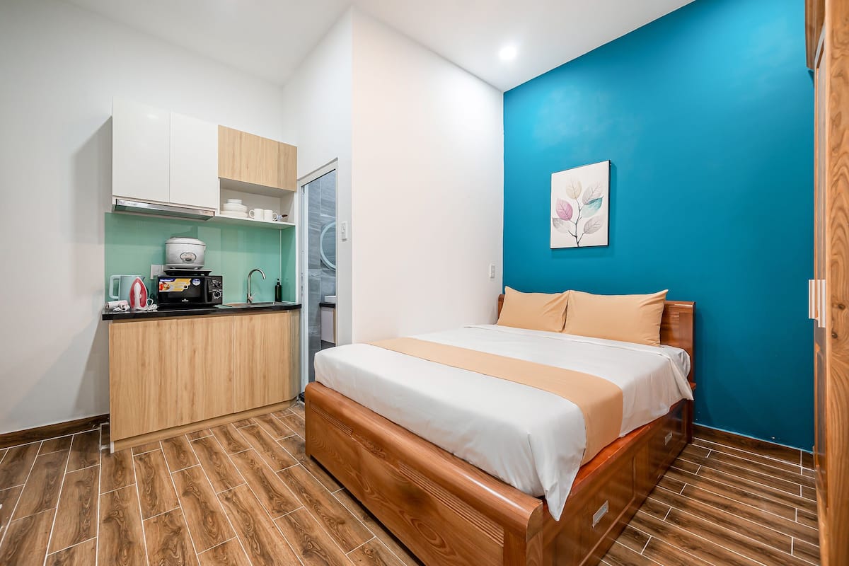 A compact room with a bed, a kitchenette, and a blue accent wall.