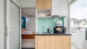 Cocina compacta con un lavamanos, microondas y armarios de madera. Se ve una cama en la habitación contigua.