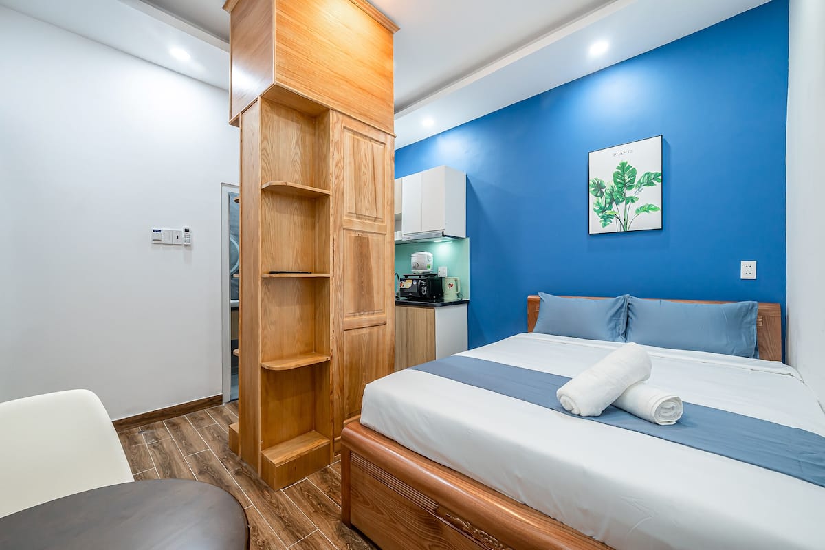 A hotel room with a bed, a wooden wardrobe, a kitchenette, and a blue accent wall.