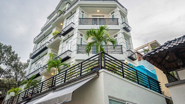 Un hotel de varios pisos con balcones, plantas en macetas y un toldo azul.