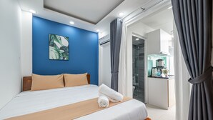 Habitación de hotel con una cama bien hecha, una pared de acento azul y vistas a la cocina y al baño a través de una puerta abierta.