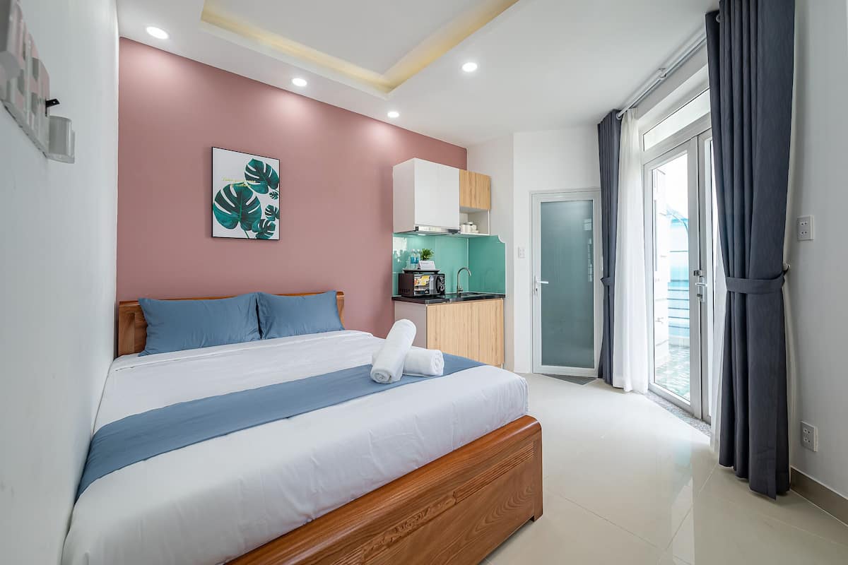 A modern bedroom with a wooden bed, a kitchenette, and a sliding glass door to the outside.