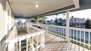 A covered deck with a railing, a table with chairs, and a view of a residential area and water. - Bayside Blessing by Miss Kitty’s (Rockport)