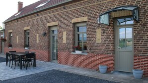Een gebouw van baksteen met een deur, ramen en een tafel met stoelen ervoor.