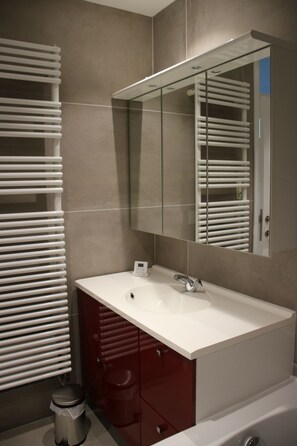Een moderne badkamer met een wit wastafel, een spiegel en een rode kast.