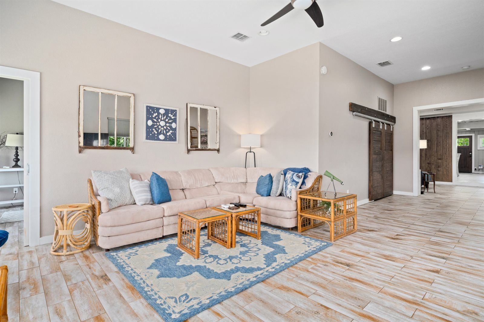 A spacious living room with a beige sofa, two side tables, a blue patterned rug, and a ceiling fan.