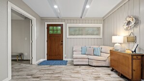 A cozy entryway with a wooden door, a cushioned bench, a blue rug, and a wooden side table with a lamp. - Knot A Care by Miss Kitty’s (Rockport)