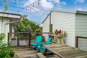 A wooden deck with two turquoise chairs and a wooden bench, a string of lights, and a wooden fence. - Knot A Care by Miss Kitty’s (Rockport)