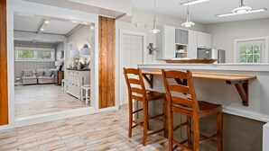 A modern kitchen with wooden chairs, a dining table, and pendant lights. - Knot A Care by Miss Kitty’s (Rockport)