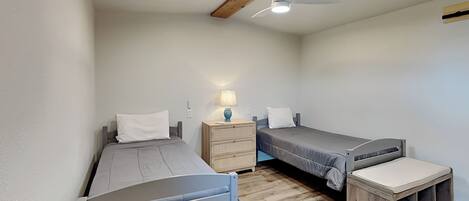A compact bedroom with two single beds, a nightstand with a lamp, a ceiling fan, and a wooden floor.