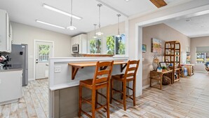 A modern kitchen with a central island, wooden chairs, and pendant lighting. - Knot A Care by Miss Kitty’s (Rockport)