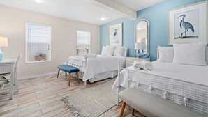 A bedroom with two beds, a desk, and a chair. There are windows with blinds, a ceiling fan, and a mirror on the wall. - Knot A Care by Miss Kitty’s (Rockport)