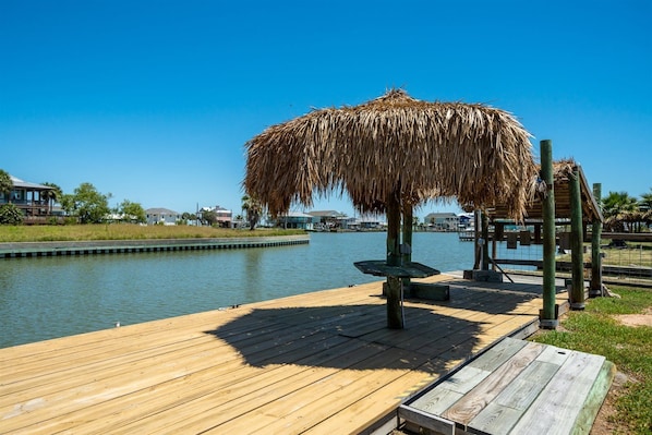 A wooden dock extending into calm water with a thatched umbrella structure. - Knot A Care by Miss Kitty’s (Rockport)