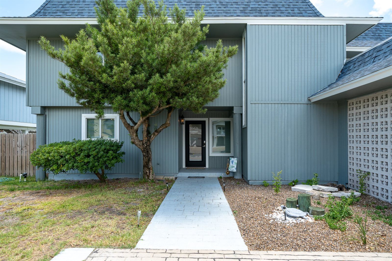 A two-story house with a grey exterior, a front door, and a tree in the front yard.
