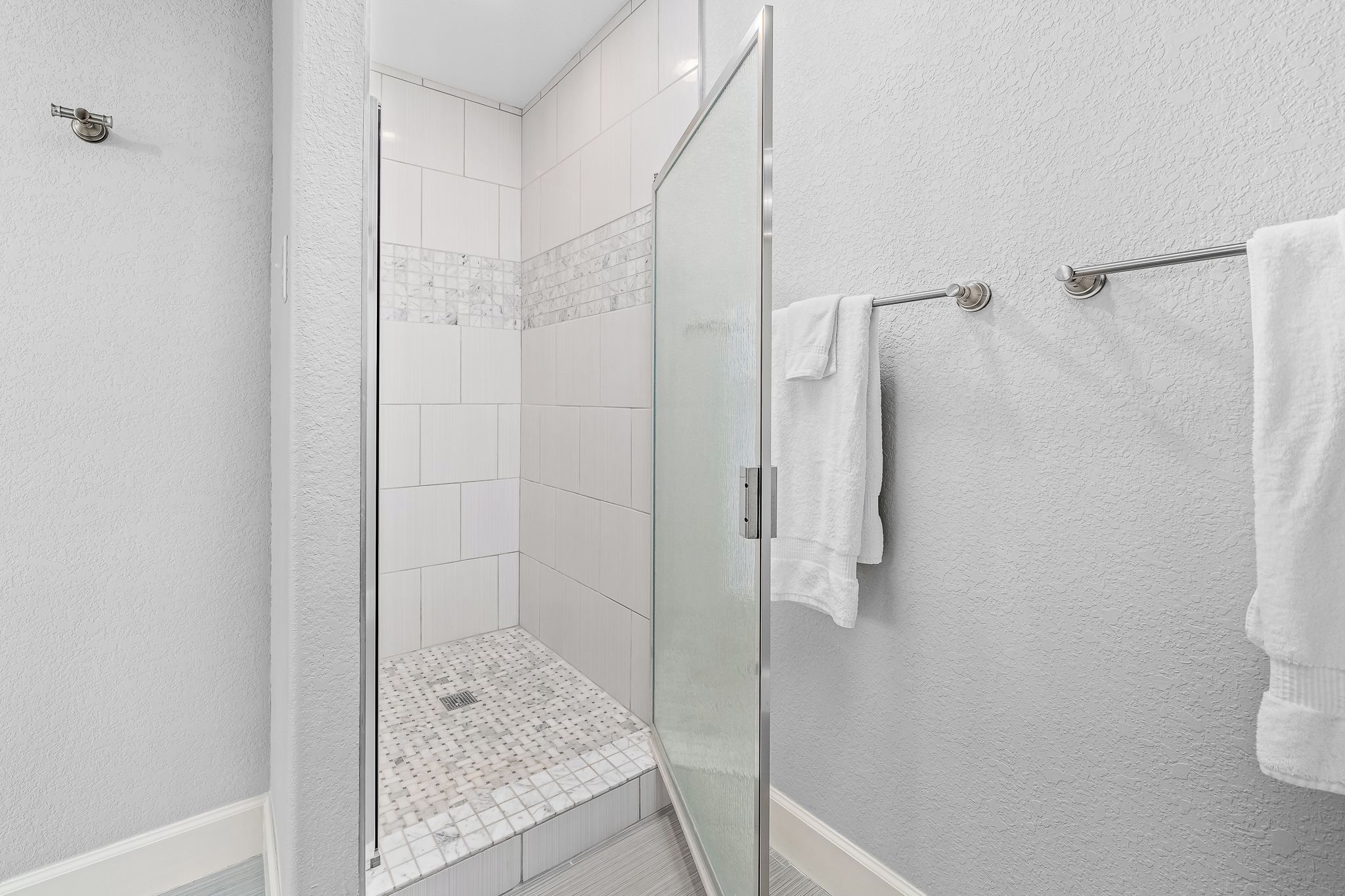 A modern bathroom with a glass shower enclosure, white tiles, and a towel rack.