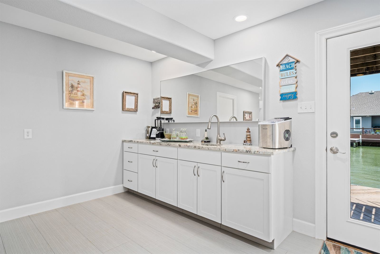 A modern kitchen with white cabinetry, a granite countertop, and a built-in oven. There are framed pictures on the wall and a sign above the sink.