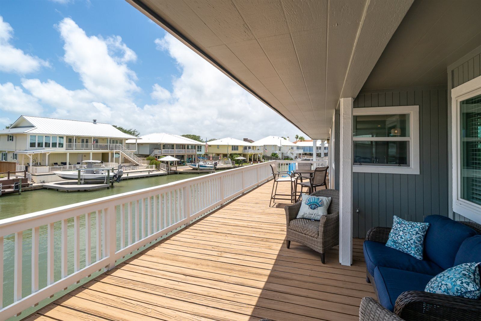 A wooden deck with a railing overlooking a marina with boats and houses.