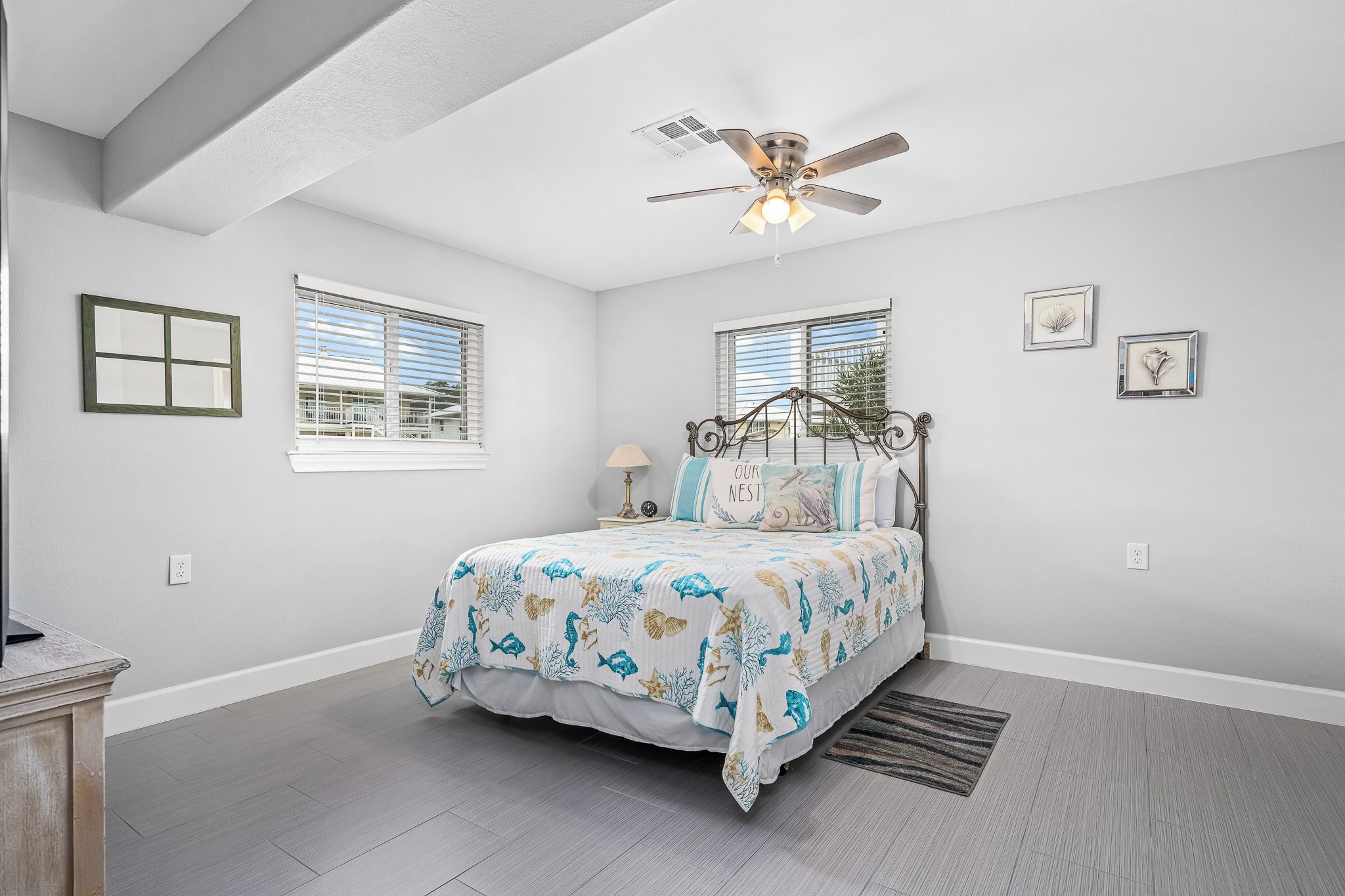 A bedroom with a bed, ceiling fan, two windows, and a nightstand.