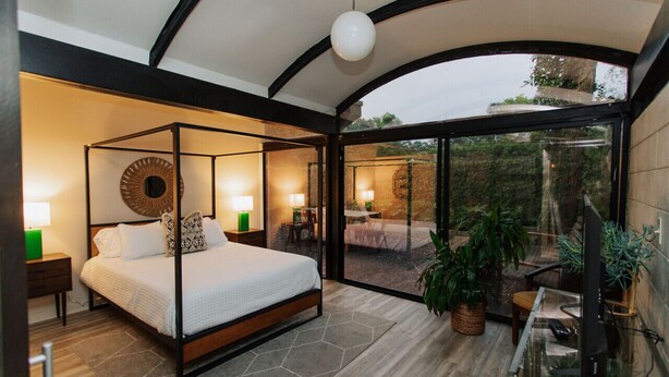 A bedroom with a four-poster bed, bedside lamps, a round mirror, and a view of an outdoor patio with seating and plants. - 2 mi from LSU! MCM Masterpiece - Sleeps 10 (Baton Rouge)
