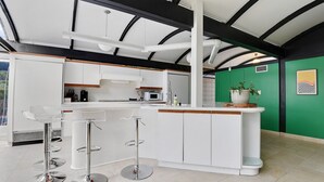 A modern kitchen with white cabinetry, a central island with stools, and a green accent wall. - 2 mi from LSU! MCM Masterpiece - Sleeps 10 (Baton Rouge)