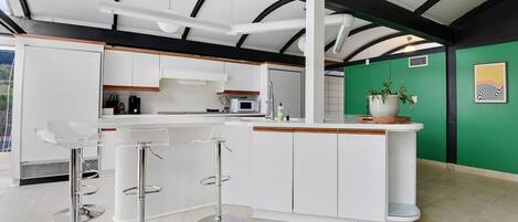 A modern kitchen with white cabinetry, a central island with stools, and a green accent wall.