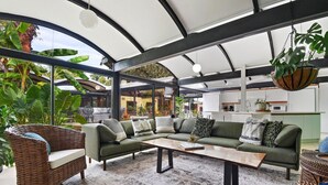 A modern living room with a sectional sofa, a hanging plant, and a large window overlooking a garden. - 2 mi from LSU! MCM Masterpiece - Sleeps 10 (Baton Rouge)
