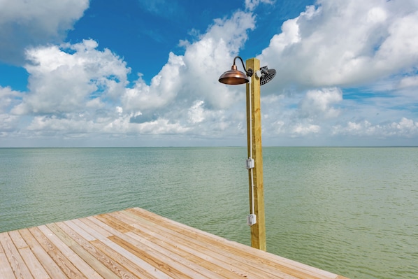 A wooden deck extending over calm turquoise water, with a metal umbrella and fan mounted on a wooden post.
