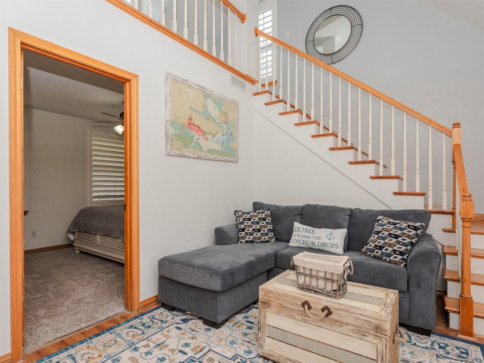 A living room with a grey sofa, a wooden chest of drawers, a patterned rug, and a staircase with wooden railings.