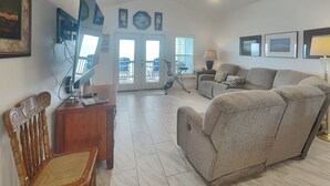 A living room with a sofa, a wooden chair, a TV, and a ceiling fan. - Copano Delight by Miss Kitty’s (Rockport)