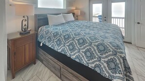 A bedroom with a bed, bedside tables, a ceiling fan, and a view of the outside balcony. - Copano Delight by Miss Kitty’s (Rockport)