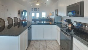A modern kitchen with white cabinetry, a large island, stainless steel appliances, and a view to the dining area. - Copano Delight by Miss Kitty’s (Rockport)