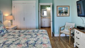 A bedroom with a bed, a chair, a dresser, a TV, and a bathroom visible through an open door. - Copano Breeze by Miss Kitty’s (Rockport)
