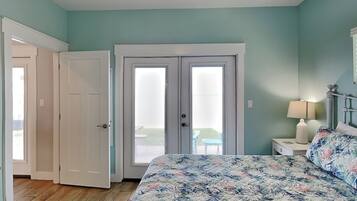 A bedroom with a bed, a nightstand, a lamp, and a view of a balcony through a door.