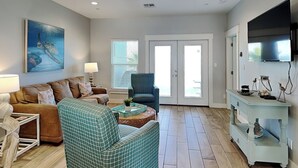 A spacious living room with a ceiling fan, a large TV, a couch, a chair, and a coffee table. - Copano Breeze by Miss Kitty’s (Rockport)
