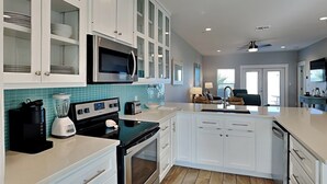 A modern kitchen with white cabinetry, a black stove, a microwave, and a blender. - Copano Breeze by Miss Kitty’s (Rockport)