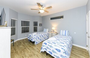 A bedroom with two beds, a ceiling fan, and a nightstand with a lamp.