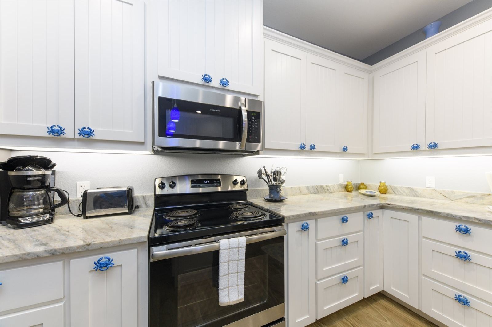 A kitchen with white cabinets, a stainless steel microwave, a stove, and a toaster.