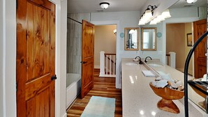 A bathroom with wooden doors, a bathtub, a vanity with two sinks, and a mirror. - Casa Del Sol by Miss Kitty’s (Rockport)