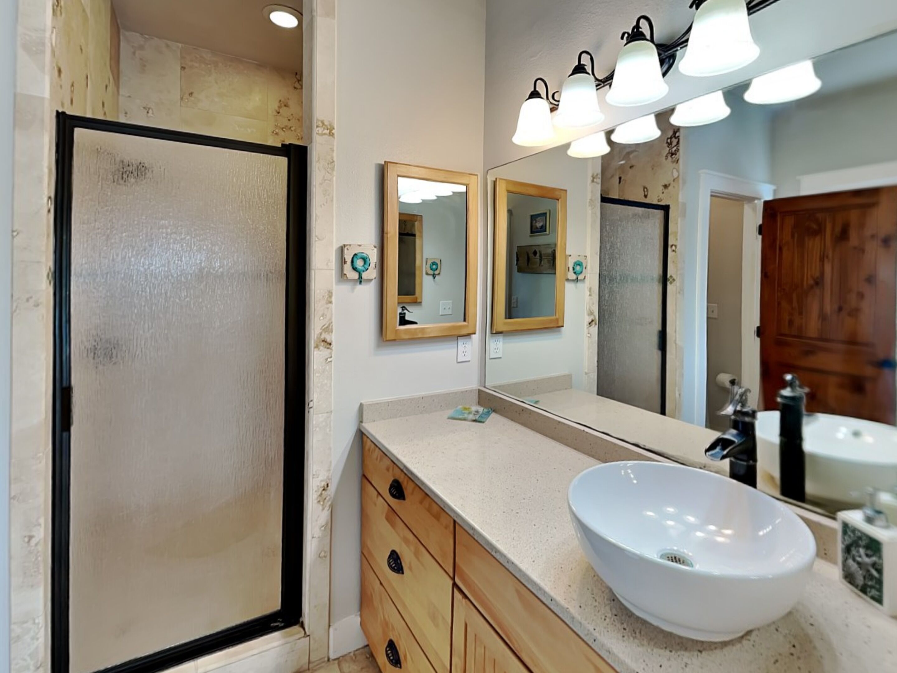 A bathroom with a large mirror, a white sink, wooden cabinets, and a shower area.