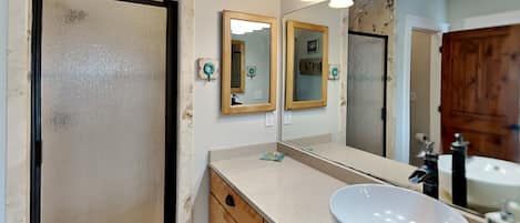 A bathroom with a large mirror, a white sink, wooden cabinets, and a shower area.