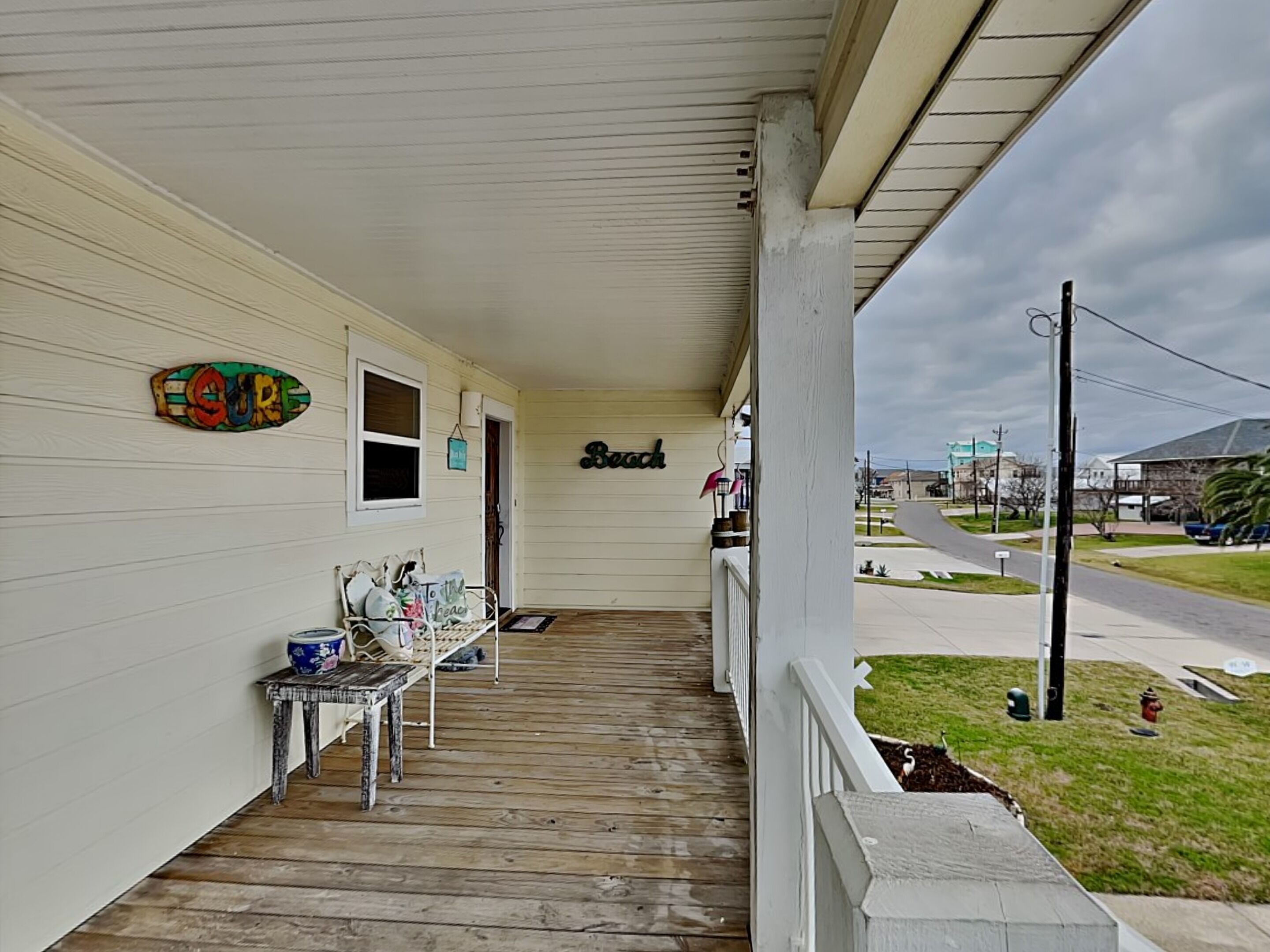 A porch with a table and chairs, a sign reading "Beach," and a view of the street.