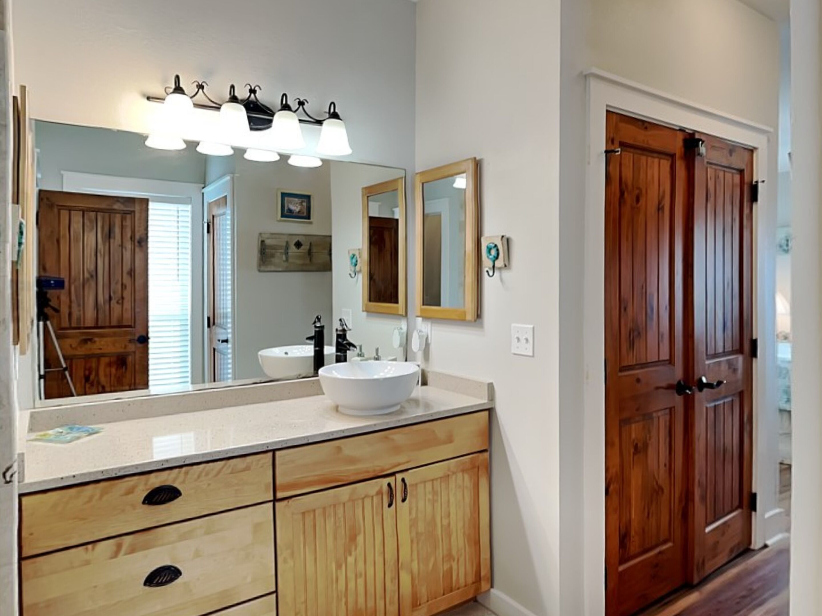 A bathroom with a large mirror, wooden cabinets, a sink, and a vanity.