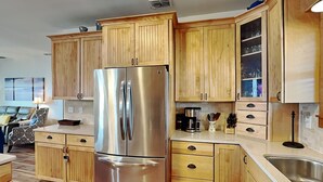 A modern kitchen with wooden cabinets, a stainless steel refrigerator, and a built-in sink. - Casa Del Sol by Miss Kitty’s (Rockport)
