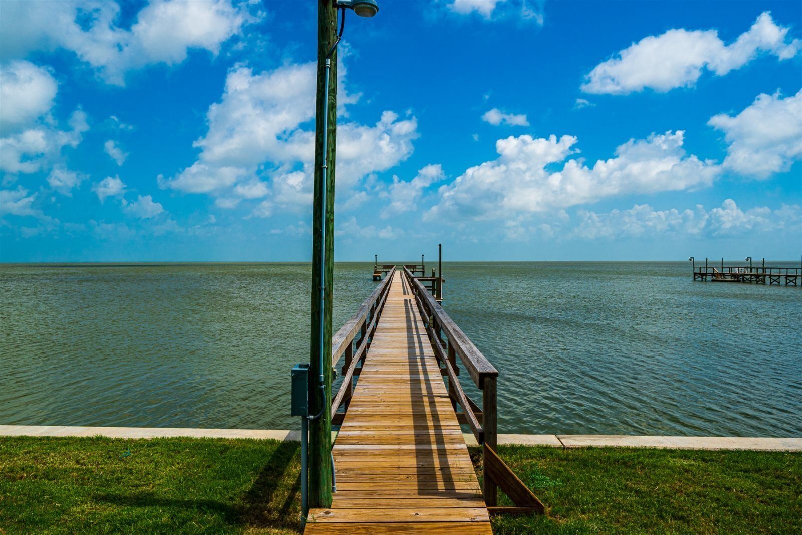 A wooden pier extending into calm waters, with a clear sky above.