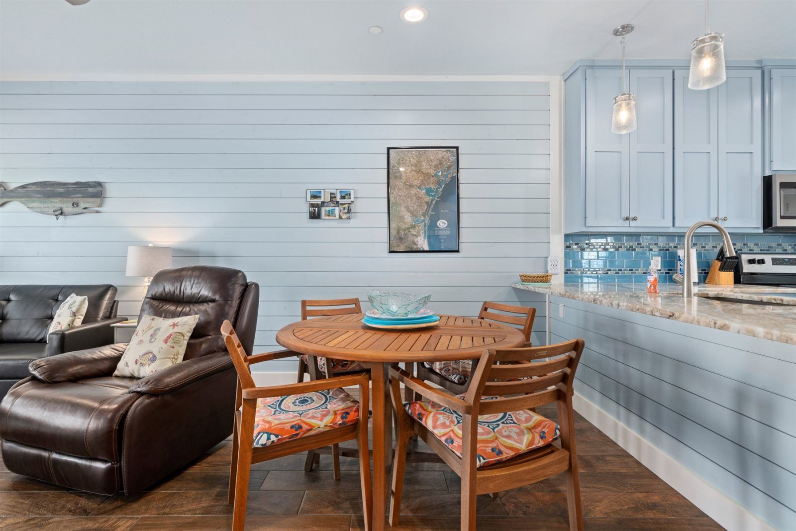 A dining area with a wooden table and chairs, a leather sofa, and a kitchen with blue cabinets and a tiled backsplash.