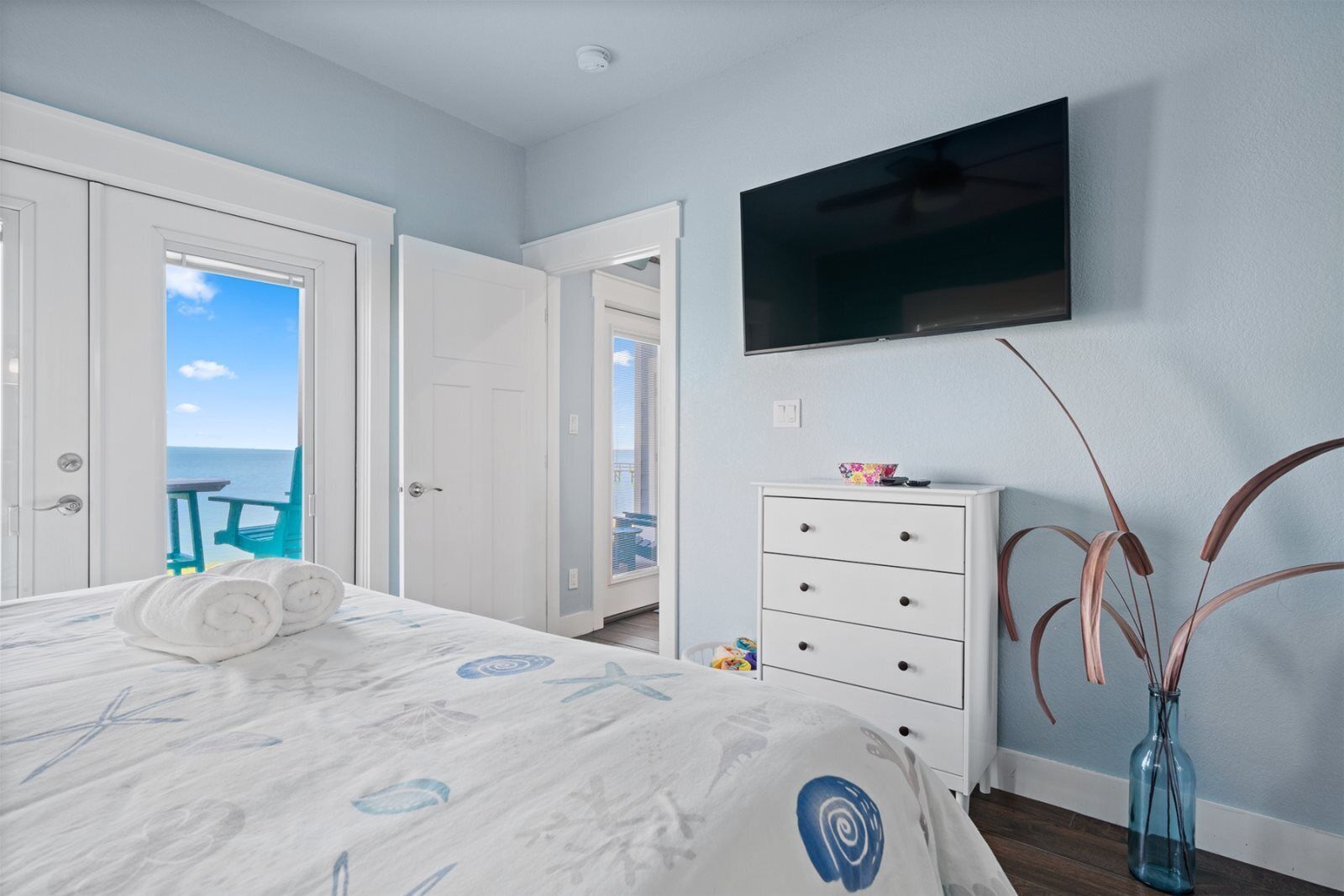 A bedroom with a bed, a dresser, a TV, and a view of the sea.
