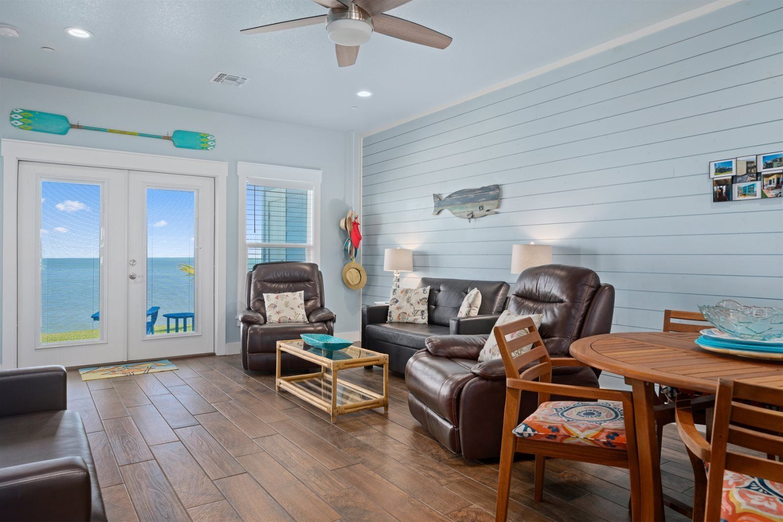 A living room with a view of the ocean, a ceiling fan, and a wooden dining table.