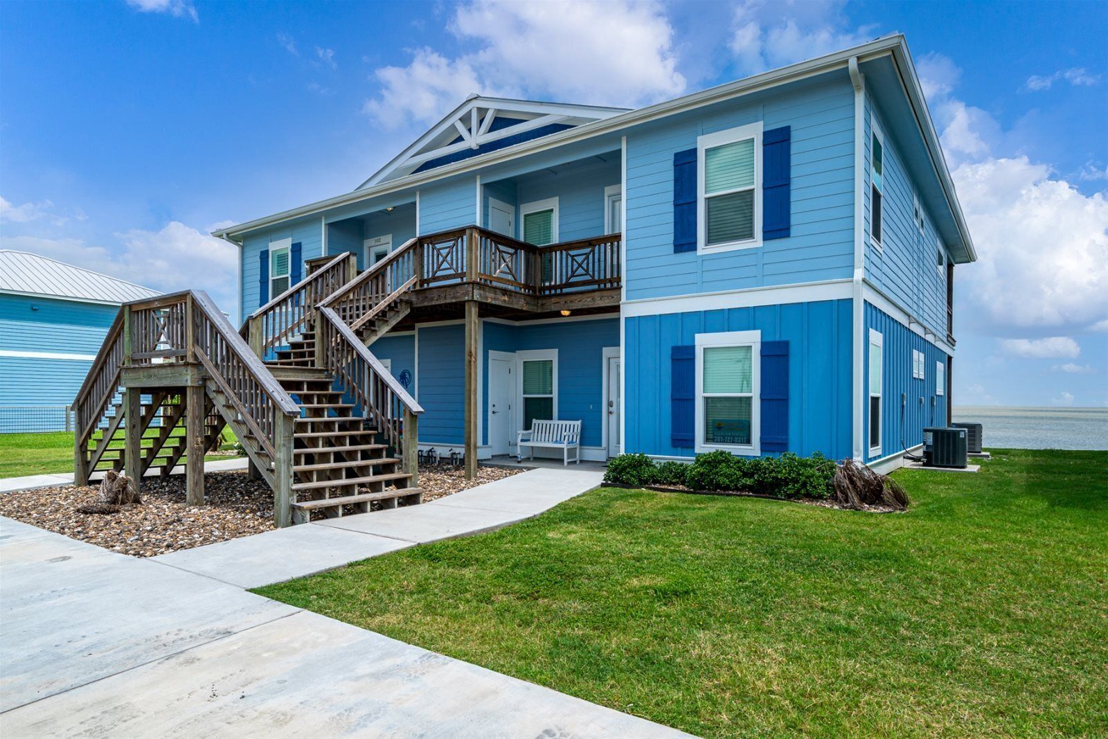 A two-story house with a wooden staircase leading to a balcony, a front porch, and a view of the ocean.
